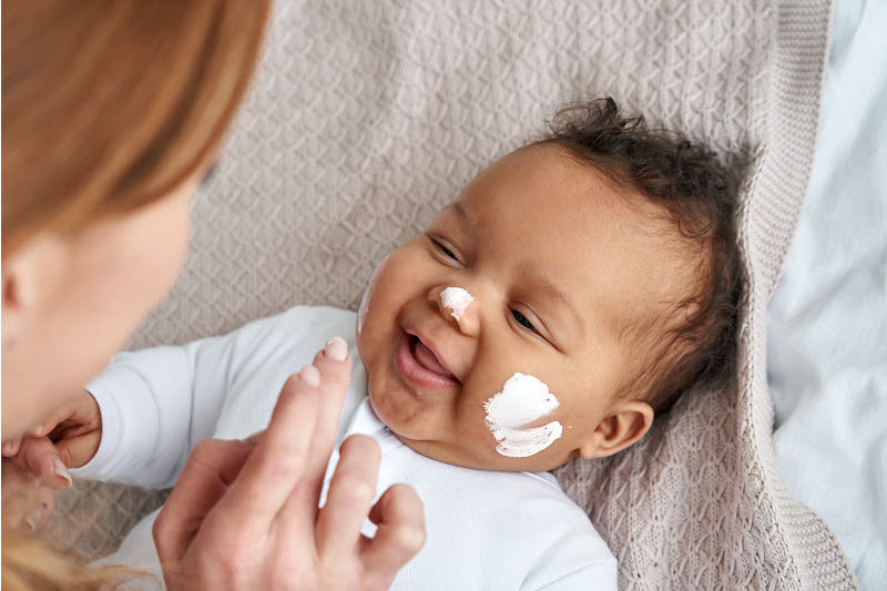 The mother is applying cream on the baby's face.