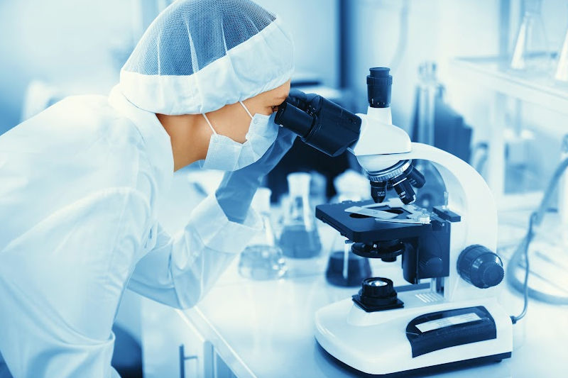 A woman is looking at a sample in a microscope. 