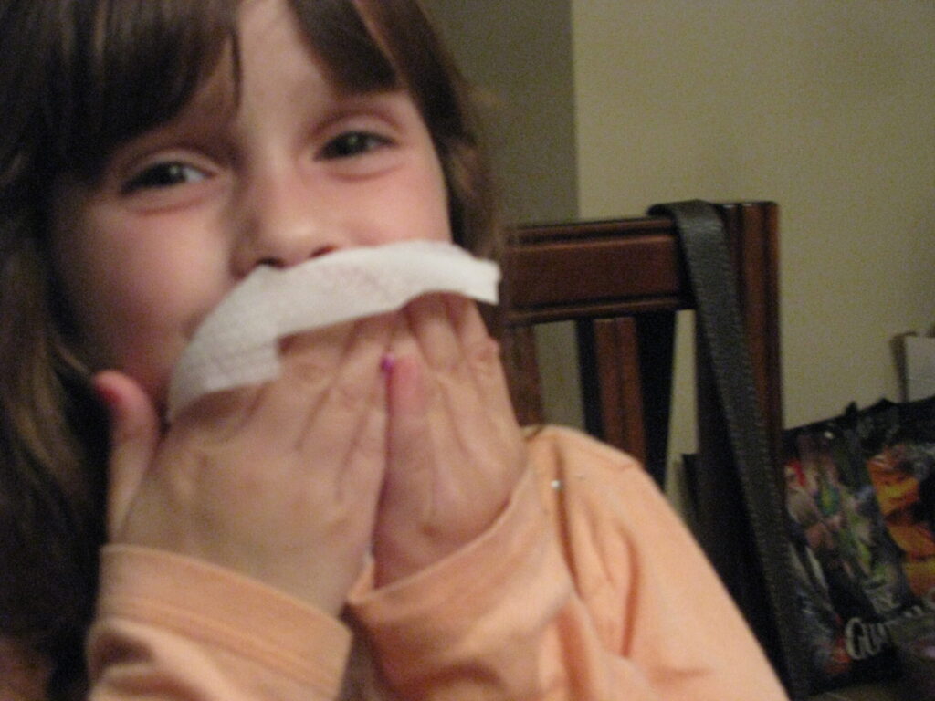 A smiling little girl is wiping her mouth with babyganics wipes.