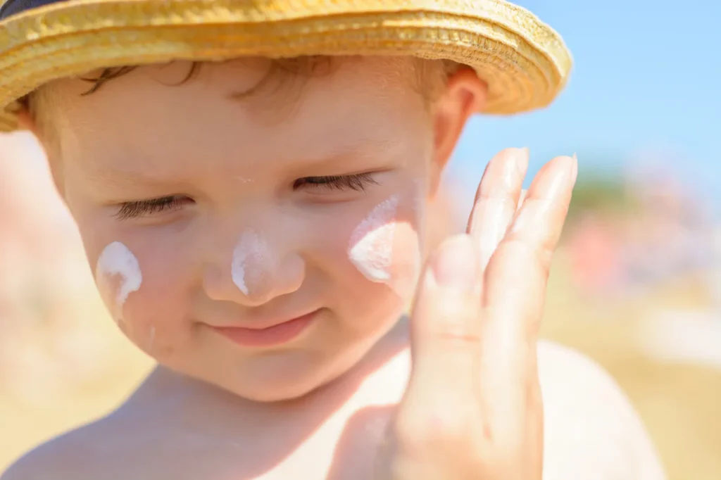A young boy with a bright smile, wearing sunscreen on his face, ready for a day in the sun.