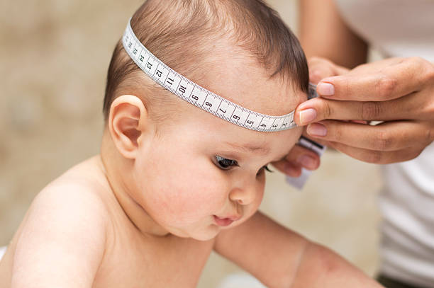 A woman measures a baby's head circumference with a soft measuring tape, focusing on the baby's head.