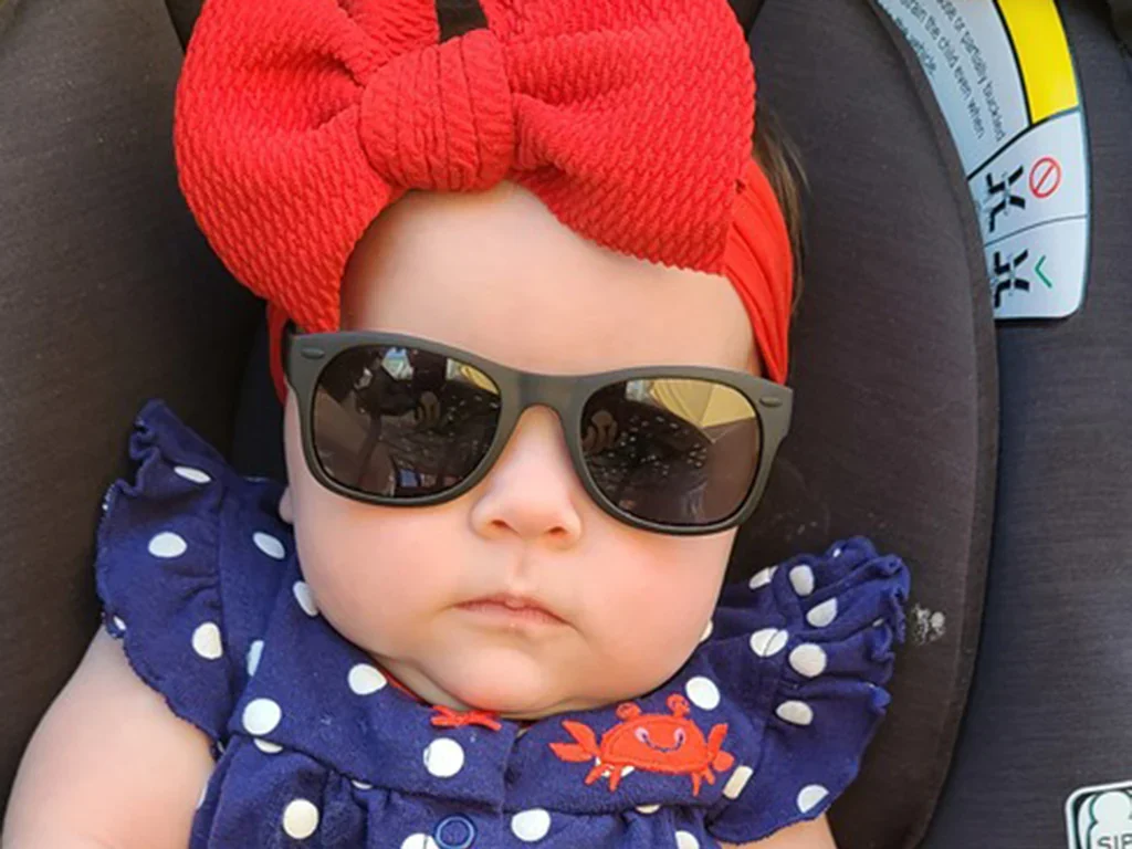 A baby girl is wearing sunglasses and sitting on a car seat