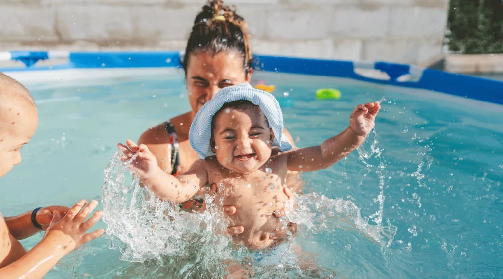 A cheerful baby is playing in water pool with her mother.