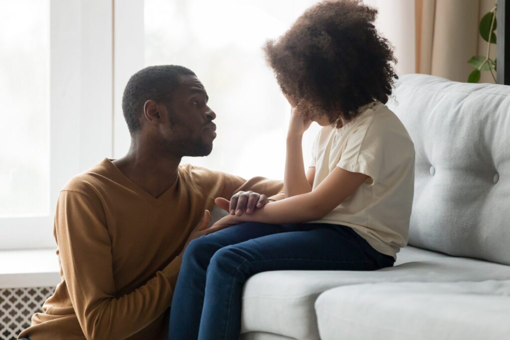 A father and daughter are sitting together on a couch, sharing a moment of relaxation and companionship.