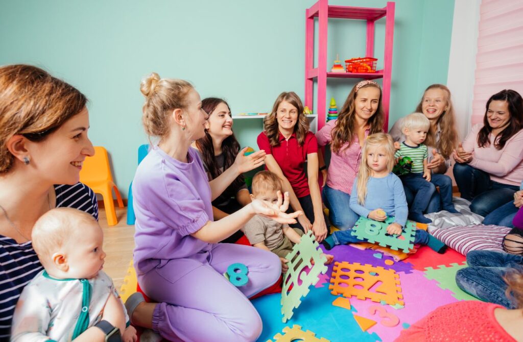 A group of women and children sitting together on the floor, engaged in conversation and sharing smiles.
