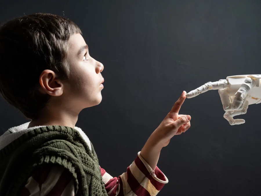 A child is trying to touch a robot's finger with his own finger.